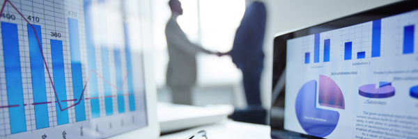 Close up of two computers with statistics and two people blurred in the background shaking hands.